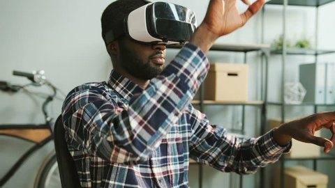 Black african man in casual shirt using vr glasses at the modern office for watching interesting video. Close up.