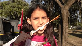 Cute little Indian girl eating candy under the tree.