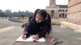 Little school girl drawing outside her school campus.