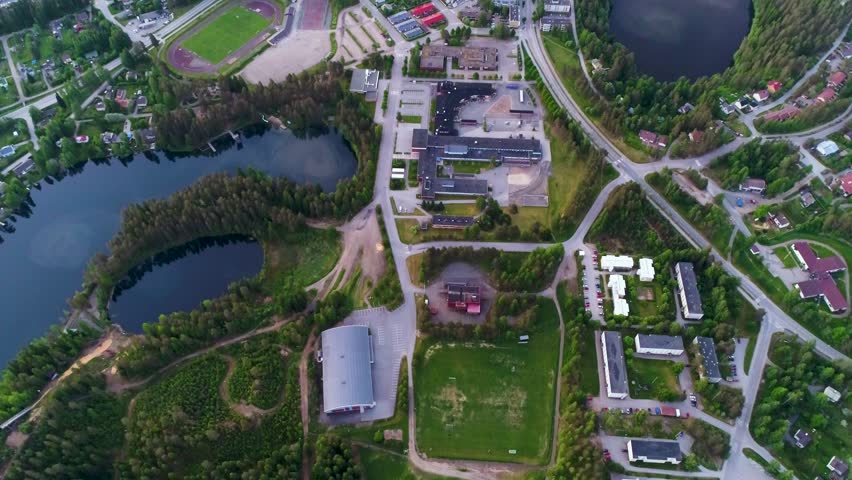 4K aerial view of small town with sport hall, power plant, houses, lakes, and forest. Camera moving from looking down to forward to horizon. Summer morning at city of Suonenjoki, Finland. Scandinavia.