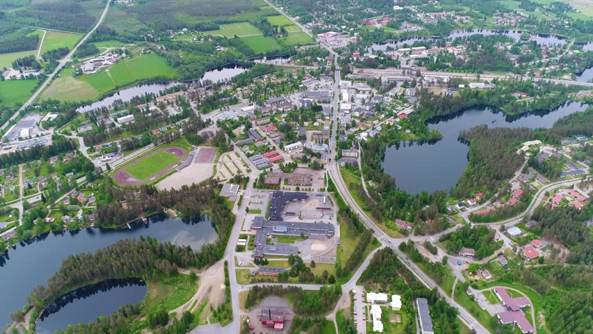 4K aerial view of small town with sport field, power plant, houses, lakes, and forest. Camera moving forward and descending. Summer early morning at city of Suonenjoki, Finland. Scandinavia.