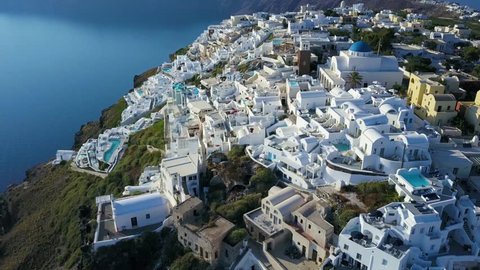 Smooth panning aerial video of Santorini, Greece, the cliff-side village of Thira, and the white buildings with blue domes. 