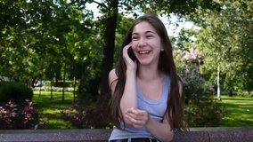 Young attractive girl speak to phone on bench. Summer park. Smile. HD video footage shooting static camera.