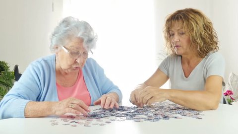 cheerful mature woman doing a puzzle and spending time with elderly senior woman at home