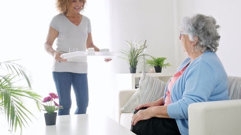 cheerful mature woman serving breakfast and taking care of a elderly senior woman at home