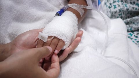 Close up of young parent and sick little daughter holding bandaged hands for comfort in a hospital bed