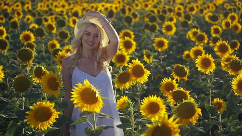 Beautiful Girl in white summer dress Outdoors. Happy Smiling Blonde Woman Enjoying Nature and Sunflowers. Ukrainian lady spinning in the Meadow. Freedom concept. Sunset. Slow motion
