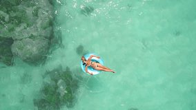 Aerial drone quad copter footage of young woman wearing virtual reality headset watching 360 travel video imagination, concept of tourist woman floating on a lilo inflatable in tropical exotic island.