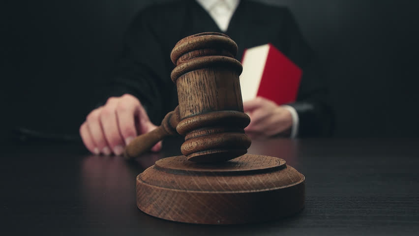 Male judge with law book in a courtroom striking the gavel