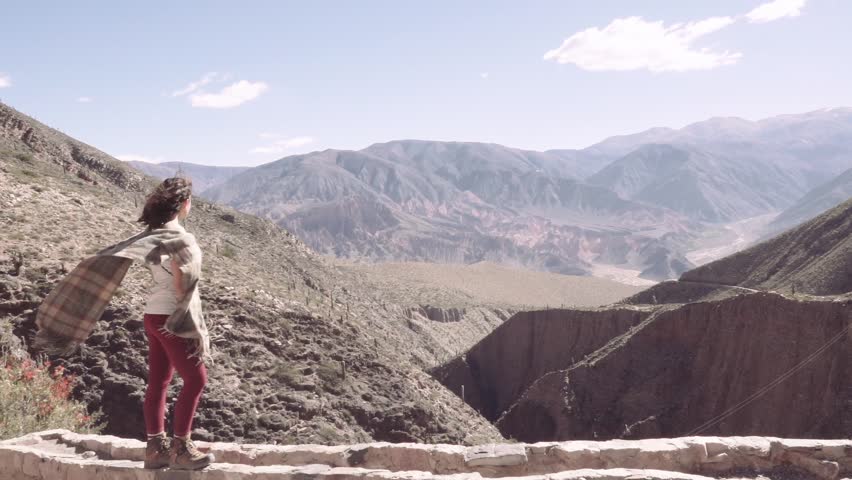 Woman walks on the edge of a cliff in a windy day, on the background the Tilcara canyon, Argentina. Slow motion