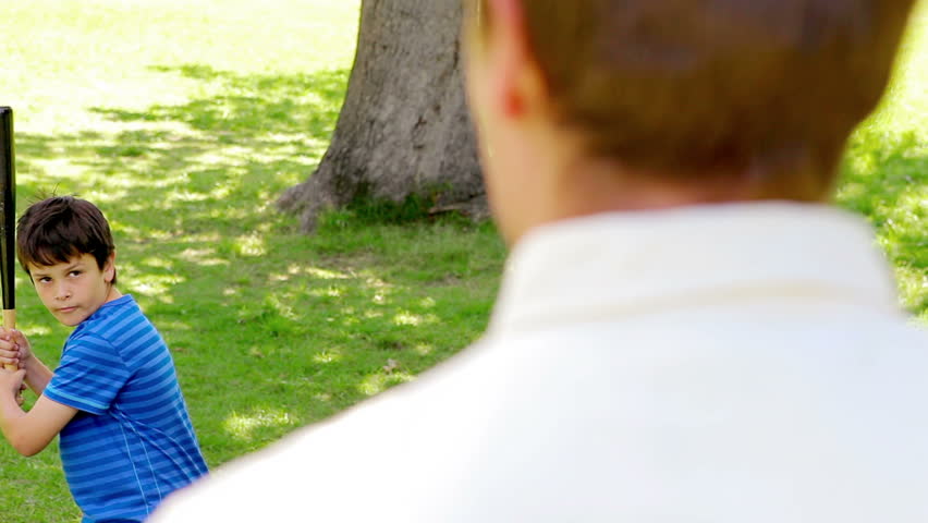 Smiling child playing baseball with his father while standing in a park