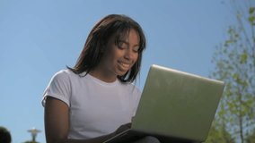 Cheerful girl in casual attire working on laptop outdoors