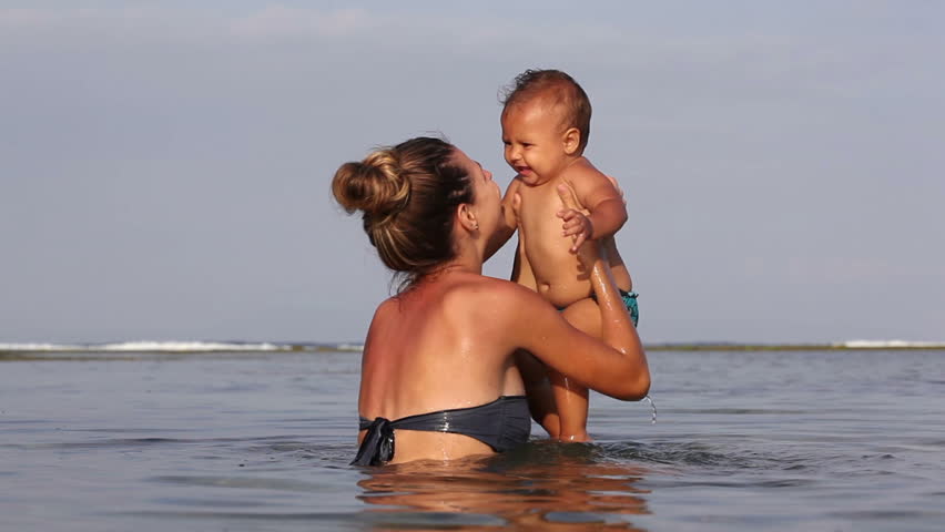 Attractive mother holds and throws up her in ocean