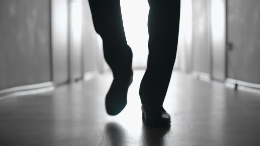 Dolly with low-section of silhouette of legs of man walking along hallway in slow motion; black and white shot Royalty-Free Stock Footage #28997251