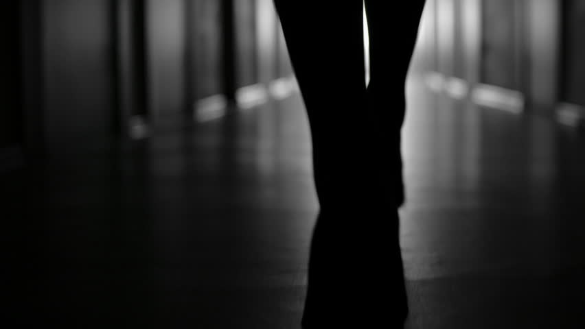 Tracking with low-section of silhouette of female legs in high heels shoes walking along dark hallway; black and white slow motion shot Royalty-Free Stock Footage #28997272