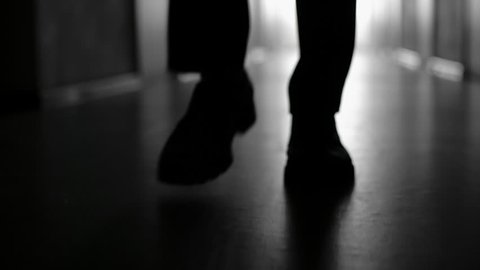Dolly with low-section of silhouette of male legs walking along hallway in slow motion; black and white shot