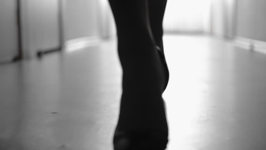 Dolly with low-section of silhouette of female legs in high heels shoes walking along corridor; black and white slow motion shot Royalty-Free Stock Footage #28997320