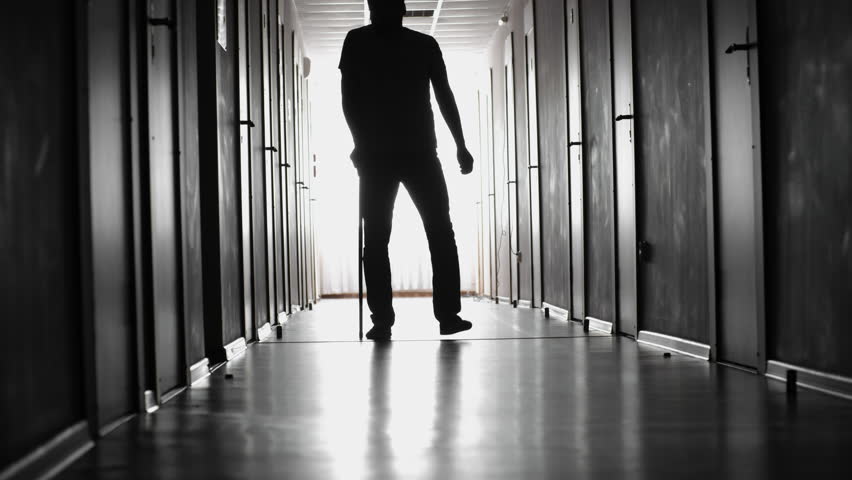 PAN of silhouette of man with walking stick limping along dark hallway of hospital towards camera | Shutterstock HD Video #28998253