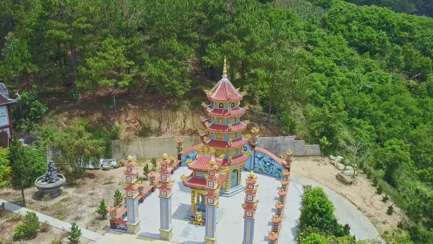 drone rotates above multilevel pagoda in traditional Buddhist temple complex among green plants in Vietnam