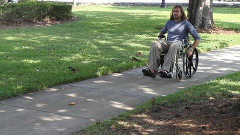 Paraplegic veteran pushes himself in his wheelchair down a sidewalk in a city park.