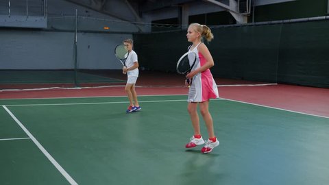 Athletic boy and girl practicing with rackets in tennis on court