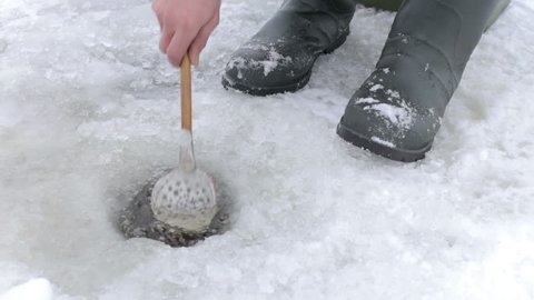 Winter fisherman cleans the workplace from unnecessary ice