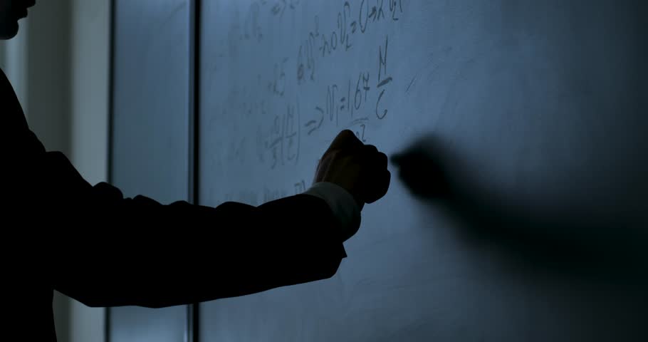 Scientist writing formulas on chalkboard. Hand with chalk wrote physics formulas on black chalkboard closeup