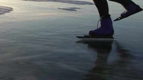 Close up view of foot of man are skating on the ice of frozen Baikal during sunset. Outdoor winter fun for athlete nice winter weather.