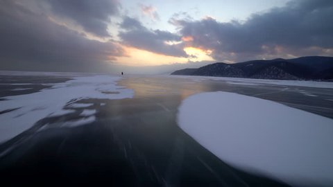Unidentified man rides his bike, on frozen lake during winter. Magnificent landscape. The sunset covered with clouds on the lake Baikal. Fast movement.