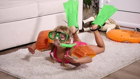 A girl in a underwater mask and flippers swimming in the room.