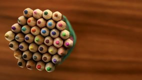 Many multicolored pencils move in a circle on a black wooden background. Concept office or school, knowledge day, the first of September. Video footage is spinning rotate