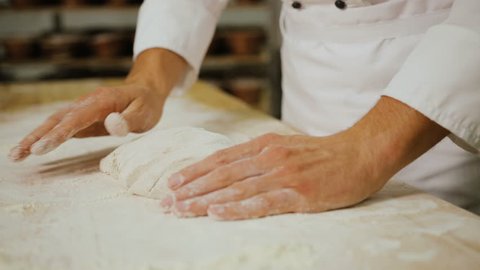 Close up shot of man hands making breads from the dough in the modern bakery background.