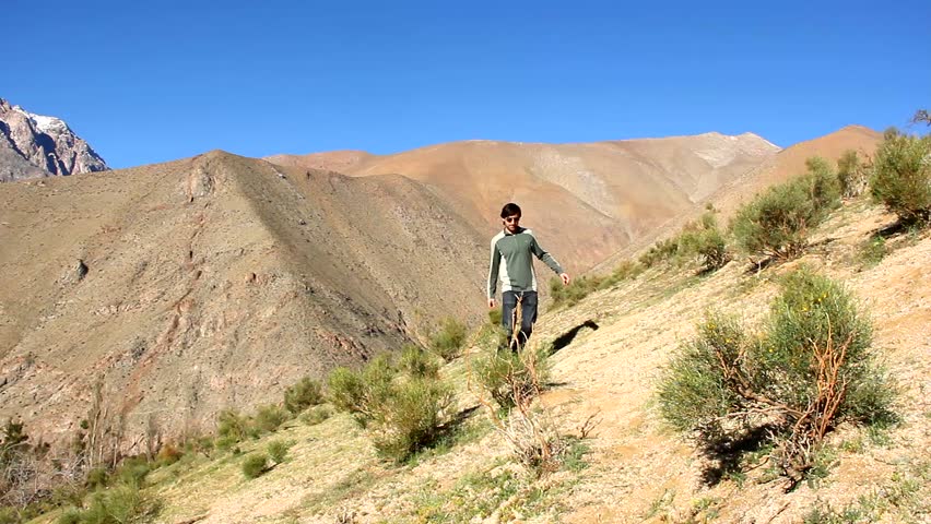 Young man with sunglasses hiking down on arid land towards the camera and passes by in Elqui Valley on sunny day, Chile