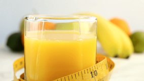 Fresh citrus fruits. Rotate Video footage of concept of healthy food and diet. Orange juice in glass wrapped in centimeter, with background of different fruits: banana, lime, lemon, orange. spinning
