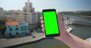 Holding a green screen smartphone in portrait mode high above the Havana, Cuba shoreline. With optional corner markers for advanced tracking.  	