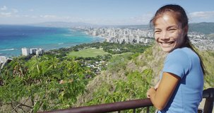 Cheerful hiker waving while standing on observation point at Diamond Head State Monument. Happy young woman is enjoying view of Waikiki Beach and Honolulu. She is wearing casuals during vacation.