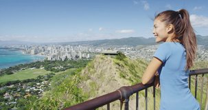 Happy hiker enjoying view of Waikiki Beach and Honolulu city. Smiling young woman is standing on observation point at Diamond Head State Monument during summer. She is wearing casuals during vacation.