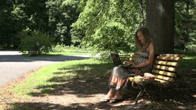 young student girl work with laptop sitting on wooden bench in green summer park outdoor. video clip.