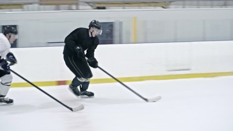 Tracking of male ice hockey forward in black uniform dribbling puck and protecting it from opposite team players, then shooting it and scoring goal