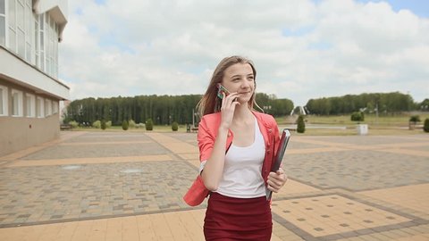Attractive young business woman walking in the park, talking on the phone.
