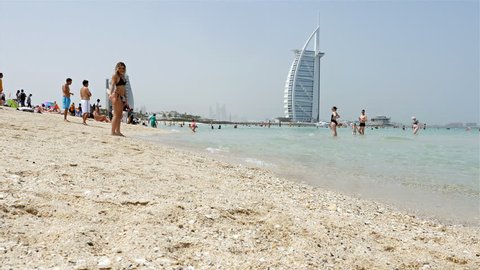 DUBAI, UNITED ARAB EMIRATES - May 5, 2017: People sunbathing in Burj al arab open beach. At the background the iconic Burj al Arab Hotel, most recognizable landmark in Dubai, United Arab Emirates