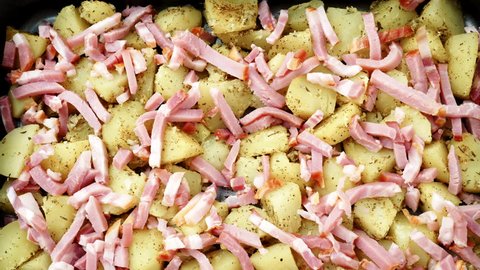 Peeled potatoes with spices, becon meat and onion slices ready to be roasted close up. Food background. Rack focus