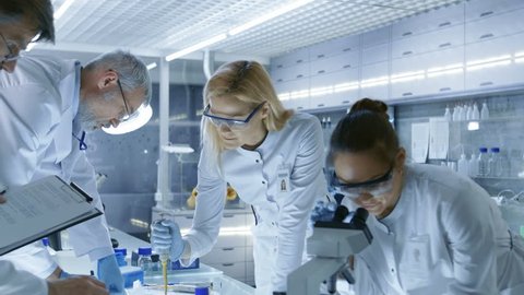 Team of Medical Research Scientists Work on a New Generation Disease Cure. They use Microscope, Test Tubes, Micropipette and Writing Down Analysis Results. Laboratory Looks Busy, Bright and Modern. 4K