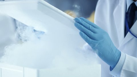 Close-up of a Medical Research Scientist Opening Refrigerator Box Takes Out Petri Dish with Samples and Examines it. He Works in a Busy Modern Laboratory Center. Shot on RED EPIC-W 8K Helium  Camera. Adlı Stok Video