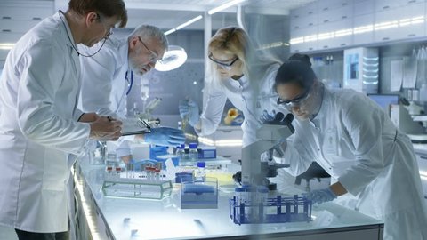 Team of Medical Research Scientists Work on a New Generation Disease Cure. They use Microscope, Test Tubes, Micropipette and Writing Down Analysis Results. Laboratory Looks Busy, Bright and Modern. 4K