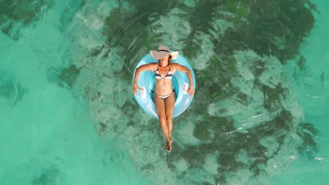 Aerial drone quad copter footage of woman floating on a lilo with hat in tropical waters of crystal clear waters of an ocean coral reef. 