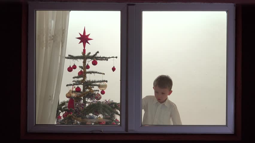 Funny child opening the window, looking for Santa Claus, Christmas tree