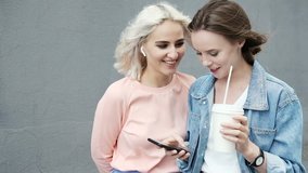 Girls amused by something they see on smart phone. Happy women using smartphone together browsing online having fun and drinking coffee