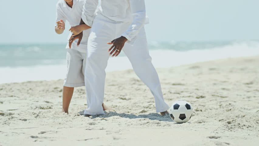 Young African American father and son playing together on beach holiday with soccer ball