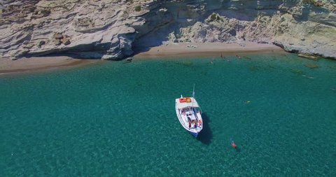 Aerial snorkeling in clear water off a white boat off a beach while on vacation in Milos Greece. Tracking backward camera wide angle bright.